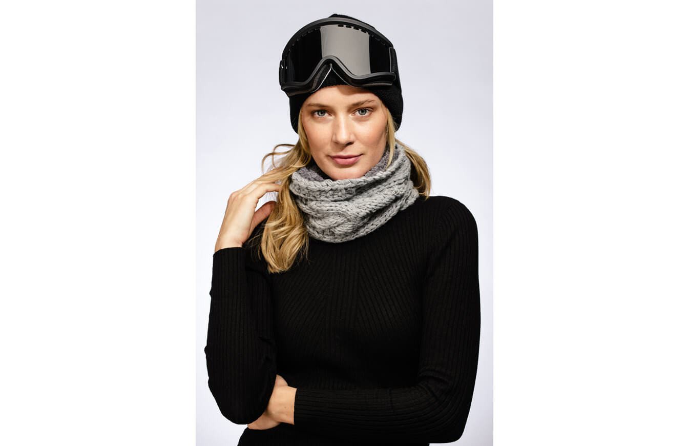 Skibrille und Neckwarmer Frau mit Skibrille und grauem Stroller Neckwarmer vor neutralem Hintergrund.