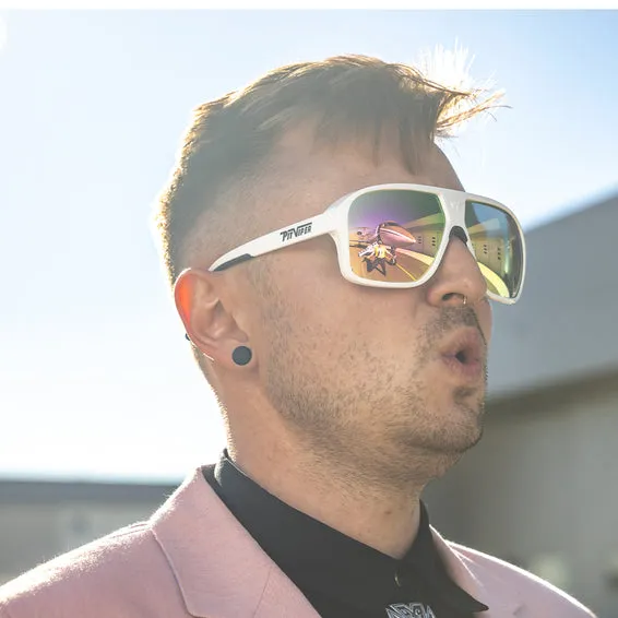 Mann mit weißer Sonnenbrille, Flugzeug spiegelt sich in den Gläsern. Er trägt einen hellrosa Blazer.