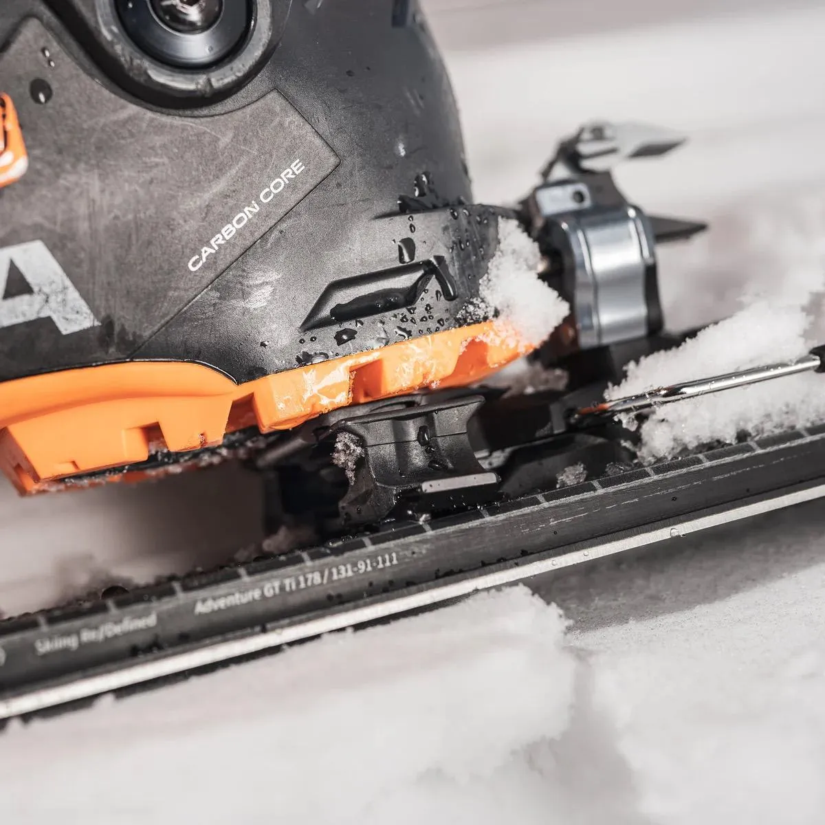 Nahaufnahme eines Skischuhs mit Carbonkern, befestigt auf einem Ski im Schnee.