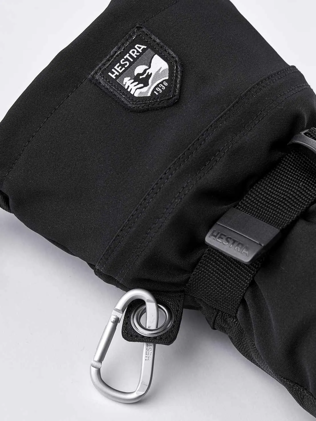 Nahaufnahme eines schwarzen Hestra Army Leather Extreme Mitt Fäustlings mit Karabiner und Logo.