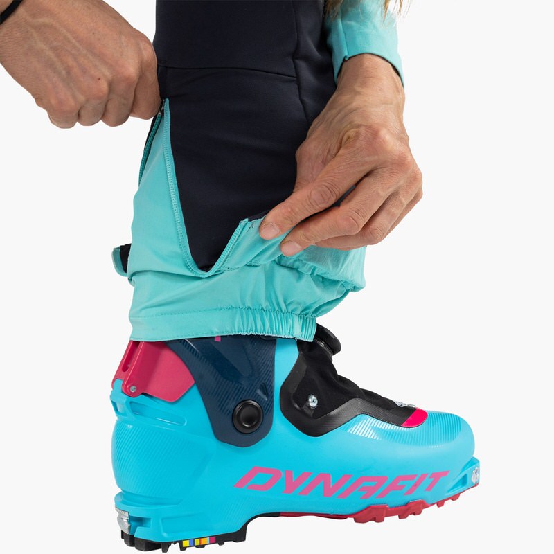 Nahaufnahme: Blaue Dynafit TLT Touring DST Damenhose, Reißverschluss am Bein über Skischuh geöffnet.
