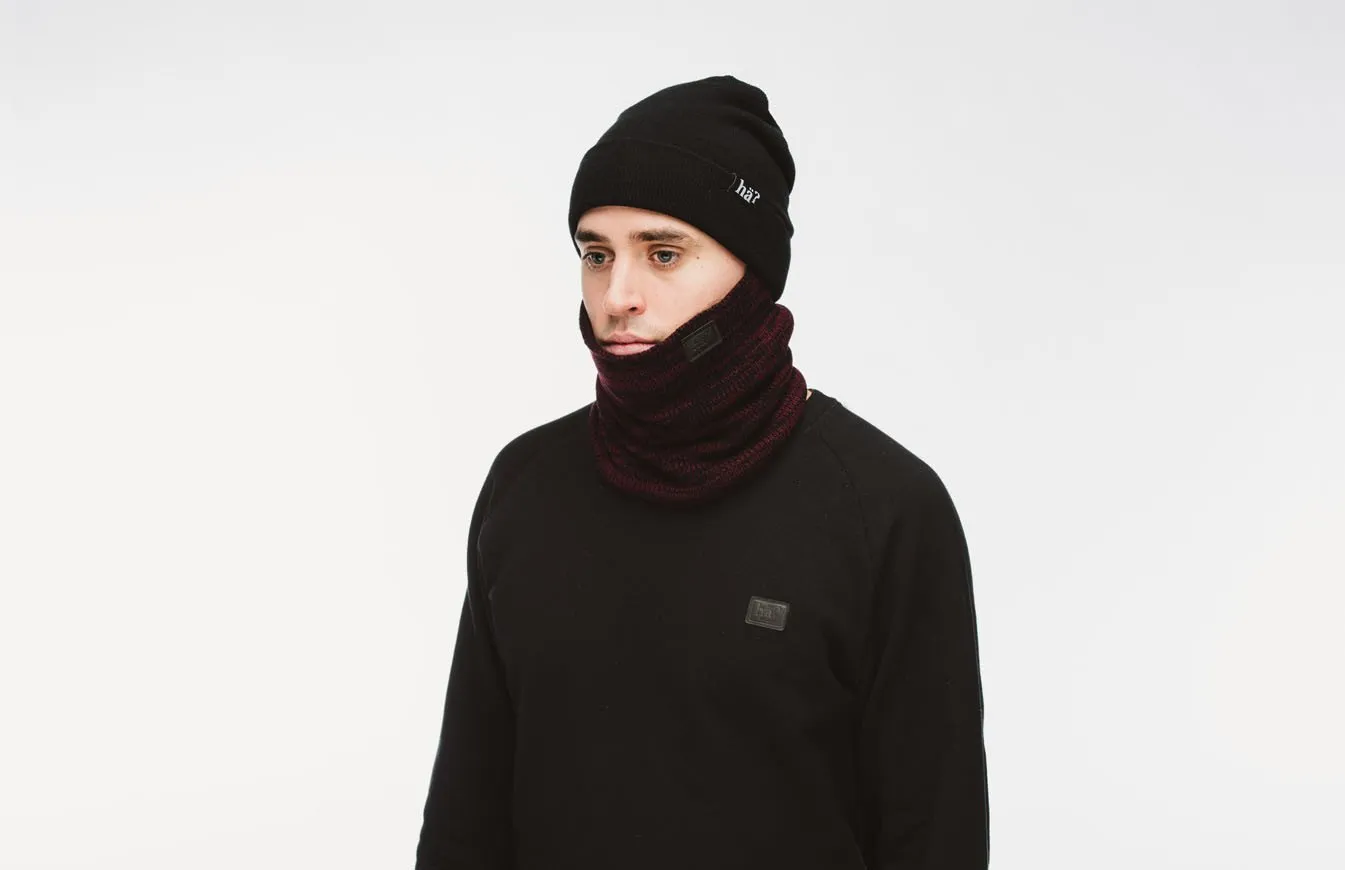 Ein Mann mit schwarzer Mütze und Melange Bordeaux Neckwarmer vor neutralem Hintergrund.