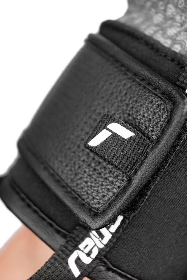 Detailaufnahme des Handgelenks eines schwarzen Reusch Marco Odermatt Handschuhs mit weißem Logo.