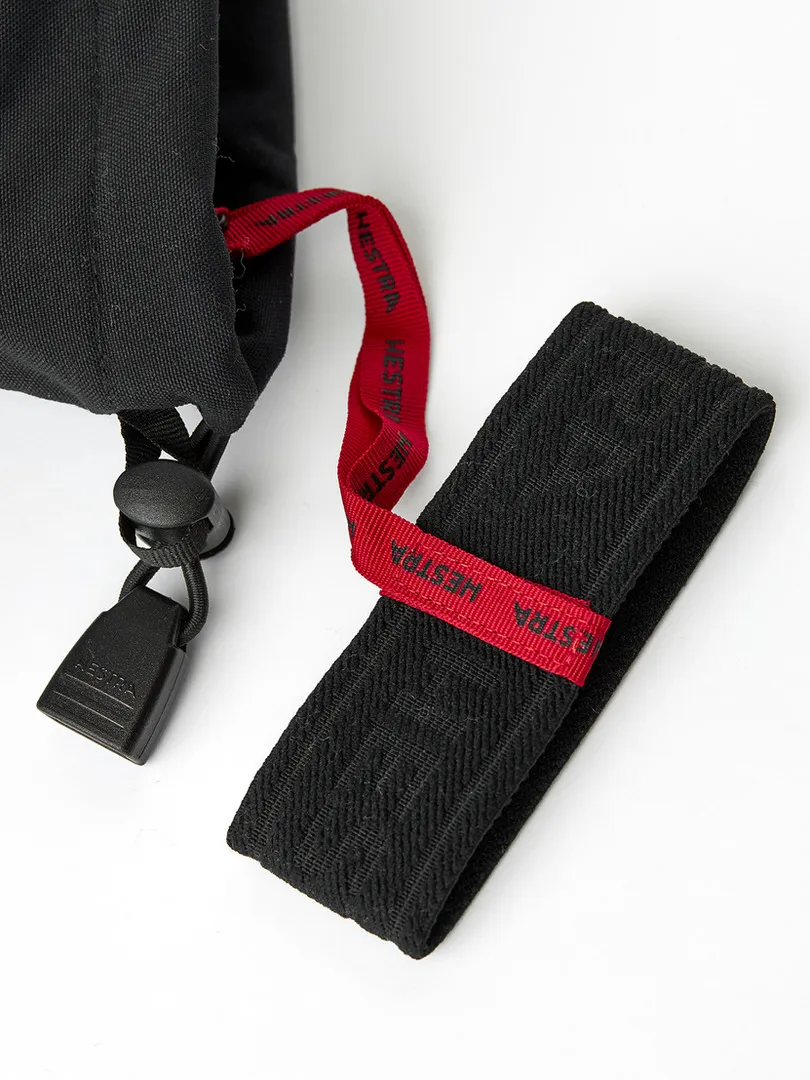 Detailaufnahme eines schwarzen Handschuhs mit Zugband und Band, jeweils mit rotem Band mit dem Aufdruck "HESTRA".