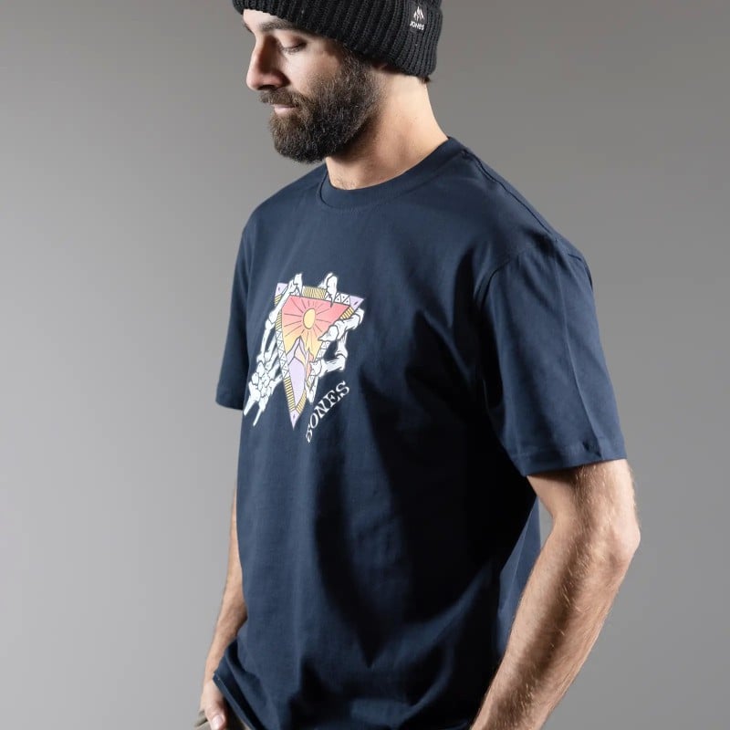 Mann mit Mütze, trägt dunkelblaues T-Shirt mit Grafikdruck: Sonne, Dreieck und Handknochen.