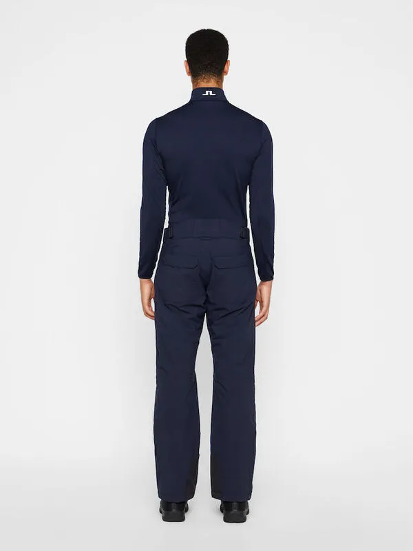 Rückansicht einer Person in marineblauen Truulli Skihose und Oberteil von J.Lindeberg vor einem weißen Hintergrund.