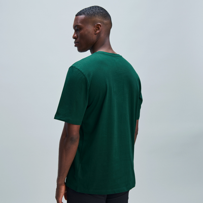 Mann im grünen T-Shirt Ein Mann mit kurzem Haar trägt ein grünes T-Shirt und schwarze Hosen, von der Seite aufgenommen.