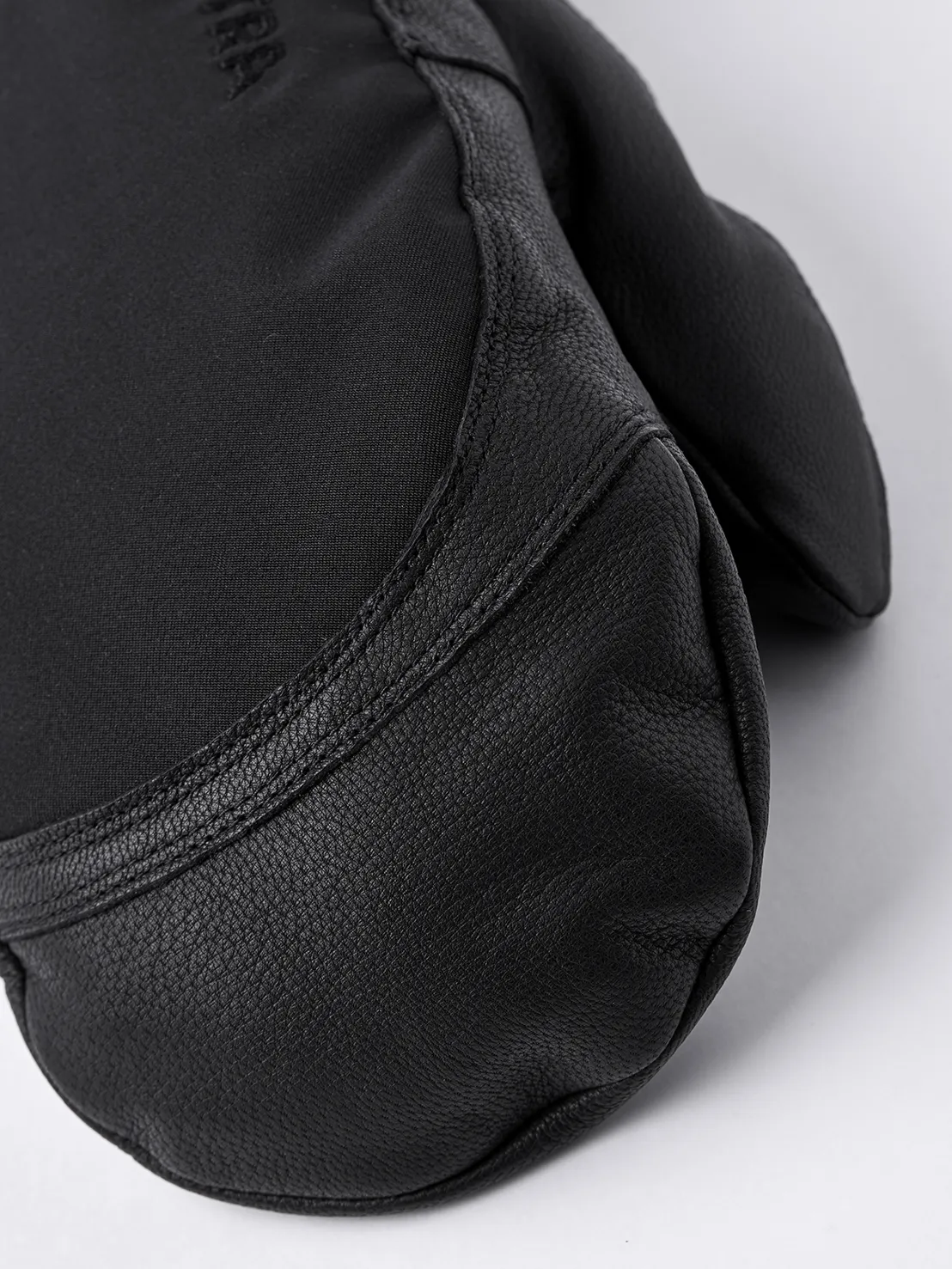 Nahaufnahme eines schwarzen Hestra Army Leather Extreme Mitt Fäustlings. Leder an der Handfläche, Textil am Handrücken.