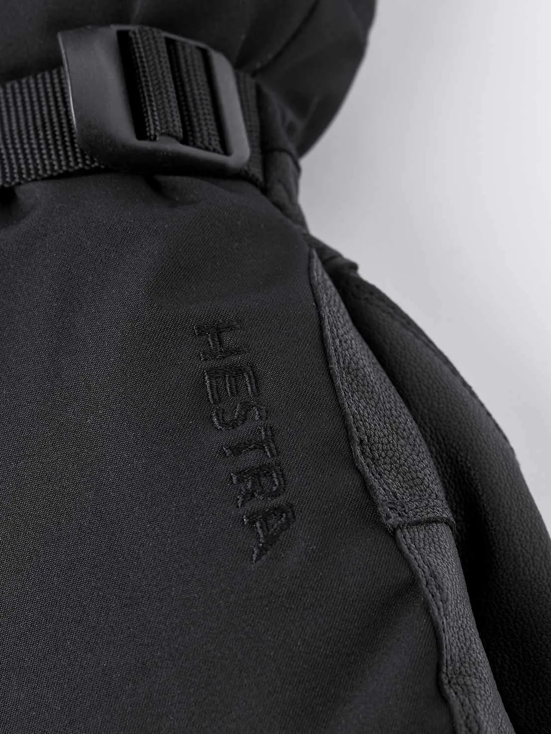 Detailansicht des schwarzen Hestra Army Leather Extreme Mitt mit Logo und Riemen.