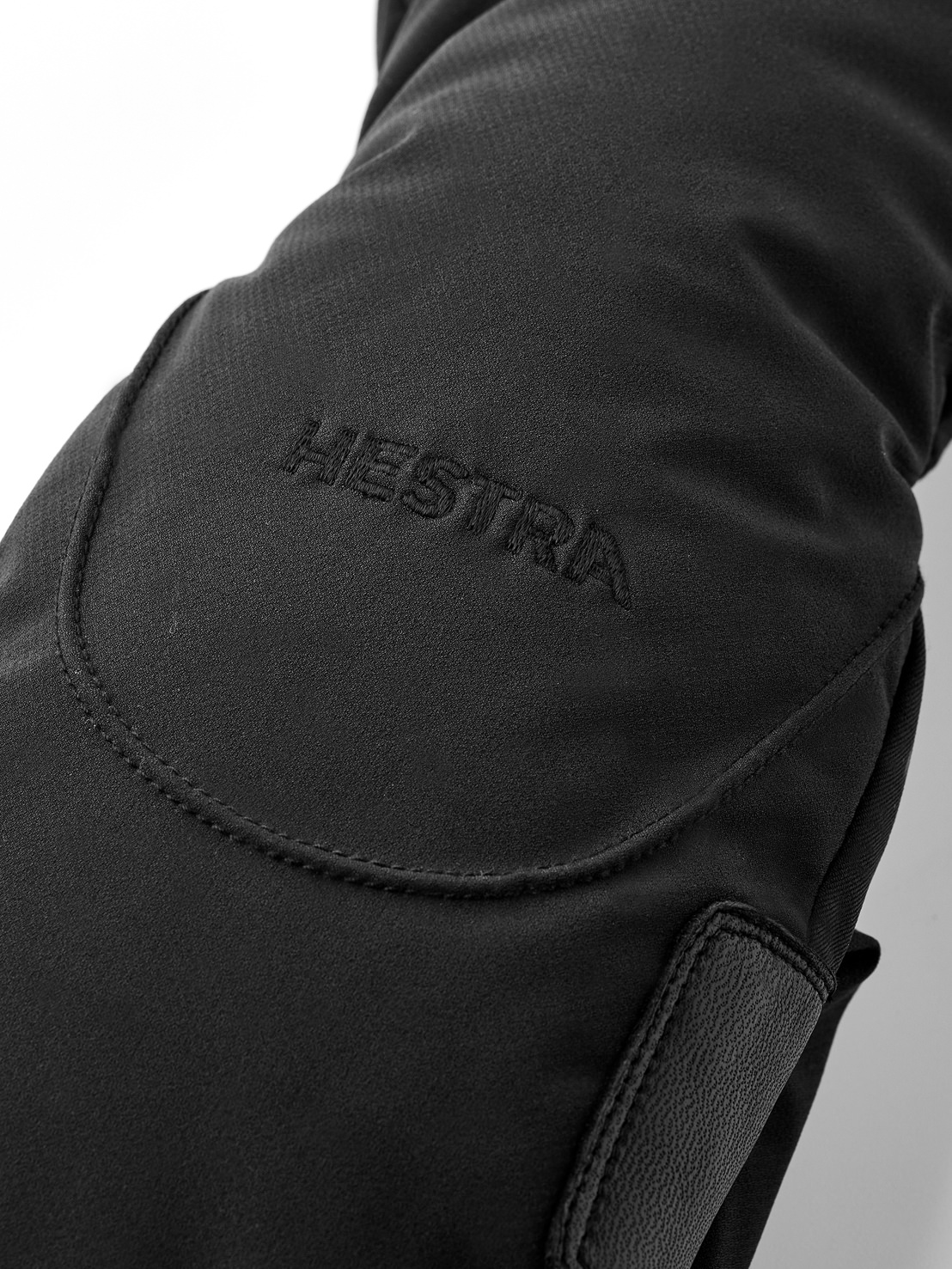 Schwarze Hestra-Handschuhe Detailaufnahme eines schwarzen Hestra-Handschuhs mit gesticktem Markennamen und Ledereinsätzen.