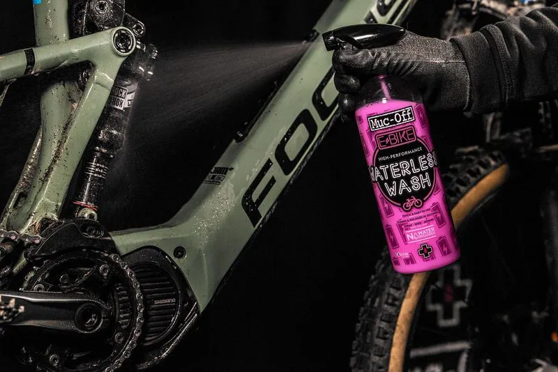 E-Bike wird mit Muc-Off Waterless Wash Reiniger eingesprüht. Pinke Sprühflasche mit der Aufschrift "Waterless Wash" ist sichtbar.
