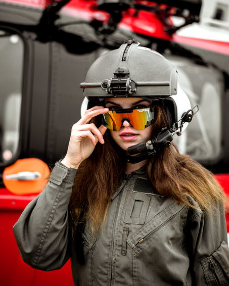 Frau mit Helm und polarisierter rosa-grauer Pit Viper Sonnenbrille vor rotem Helikopter.