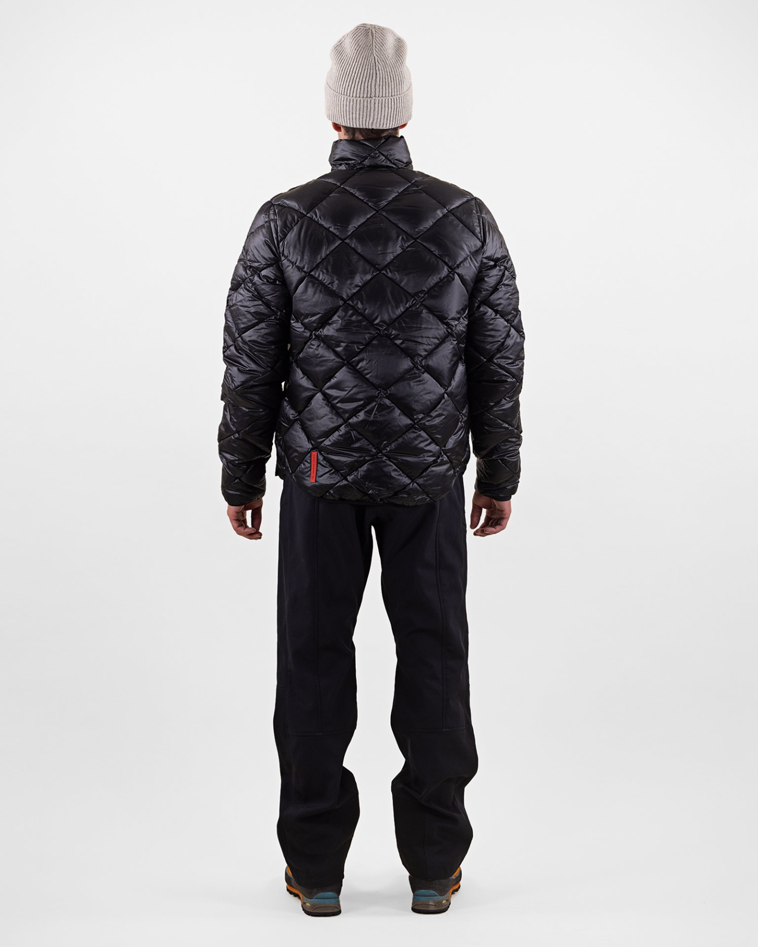 Person von hinten, trägt schwarze Daunenjacke mit Rautenmuster, Hose und Mütze.