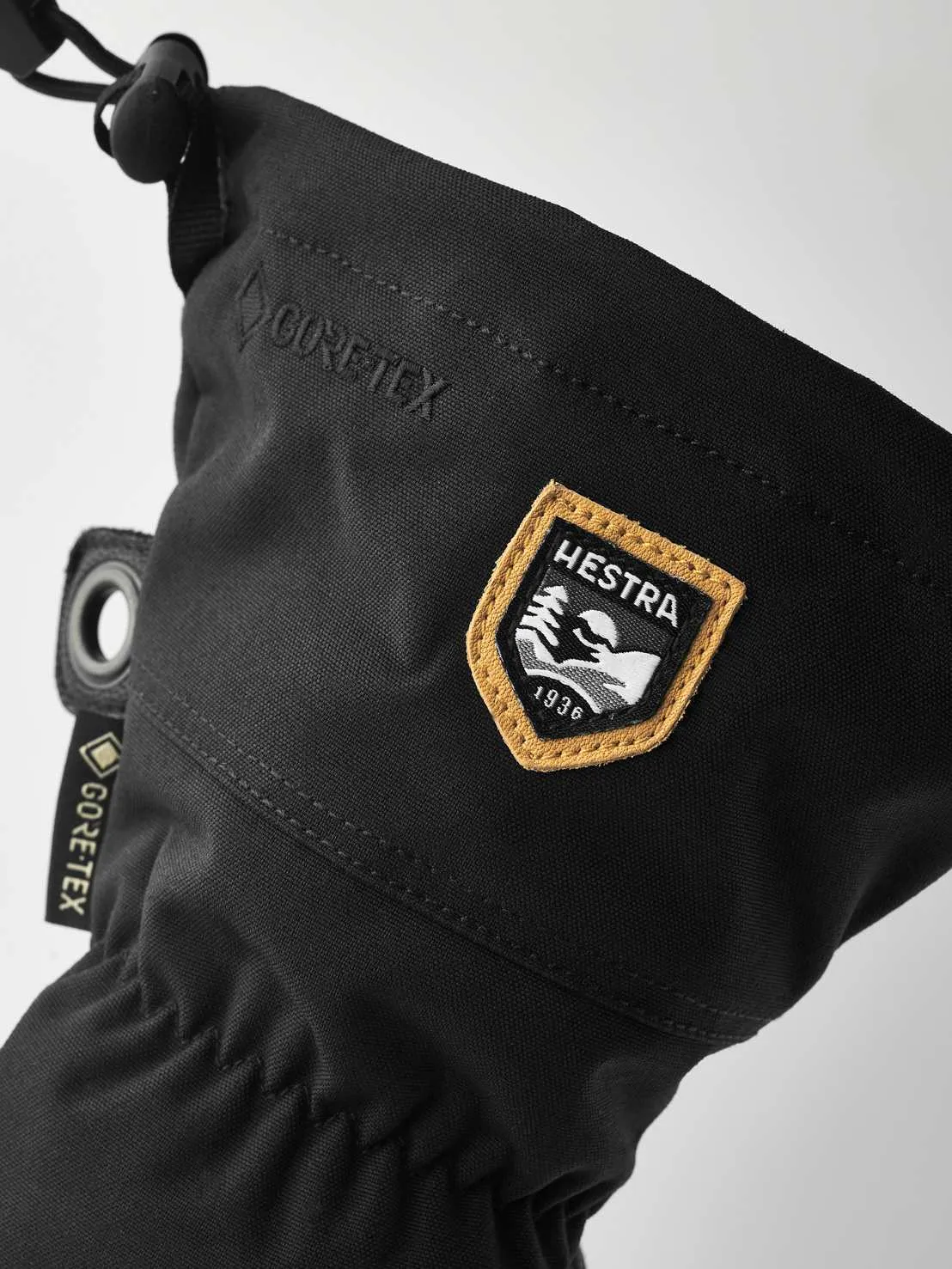 Detailaufnahme eines schwarzen Hestra Army Leather Gore-Tex Fäustlings mit Logos und Zugschnur.