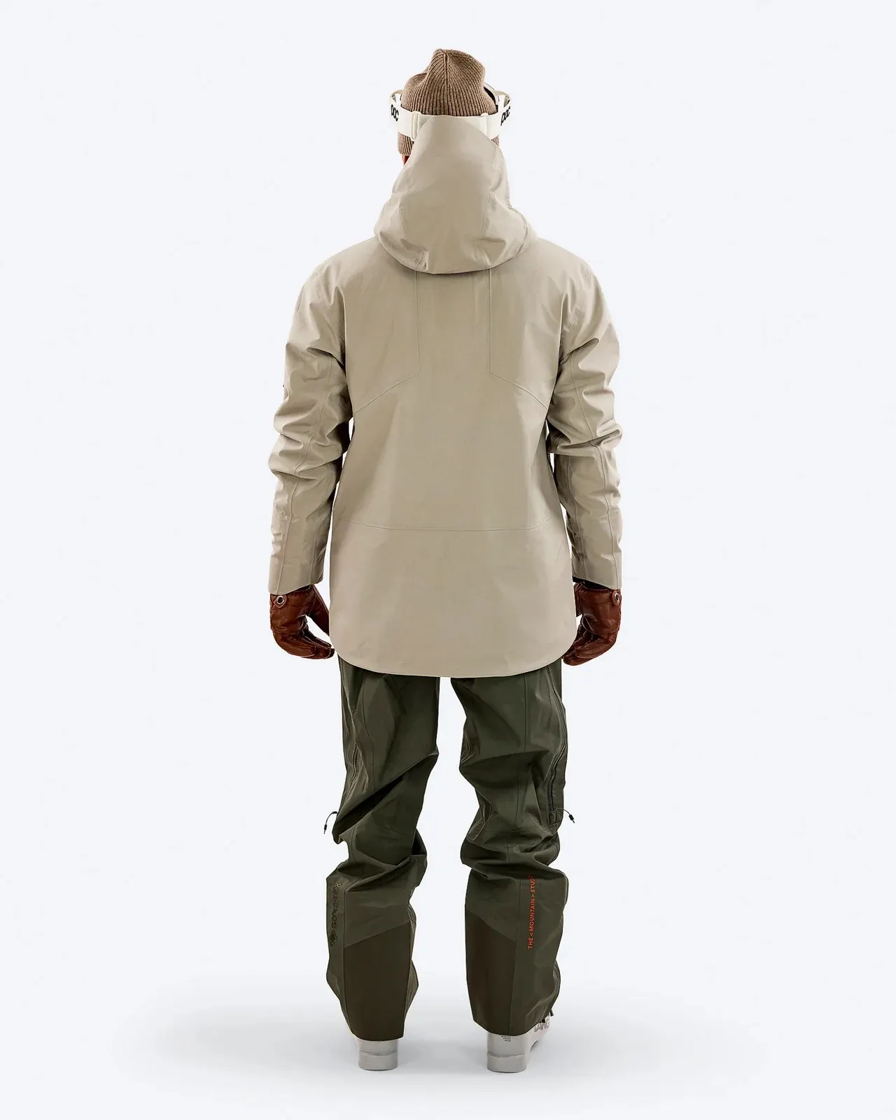 Rückansicht: Beige Z-2 EPE Jacke und grüne Hose, Teil eines Ski-Outfits mit Mütze und Skibrille.