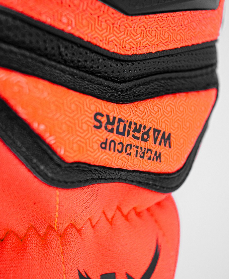 Reusch Worldcup Warrior SC Detailansicht eines Reusch Worldcup Warrior SC Handschuhs mit orangenem Muster und schwarzer Naht. Der Text "WORLDCUP WARRIORS" ist sichtbar.