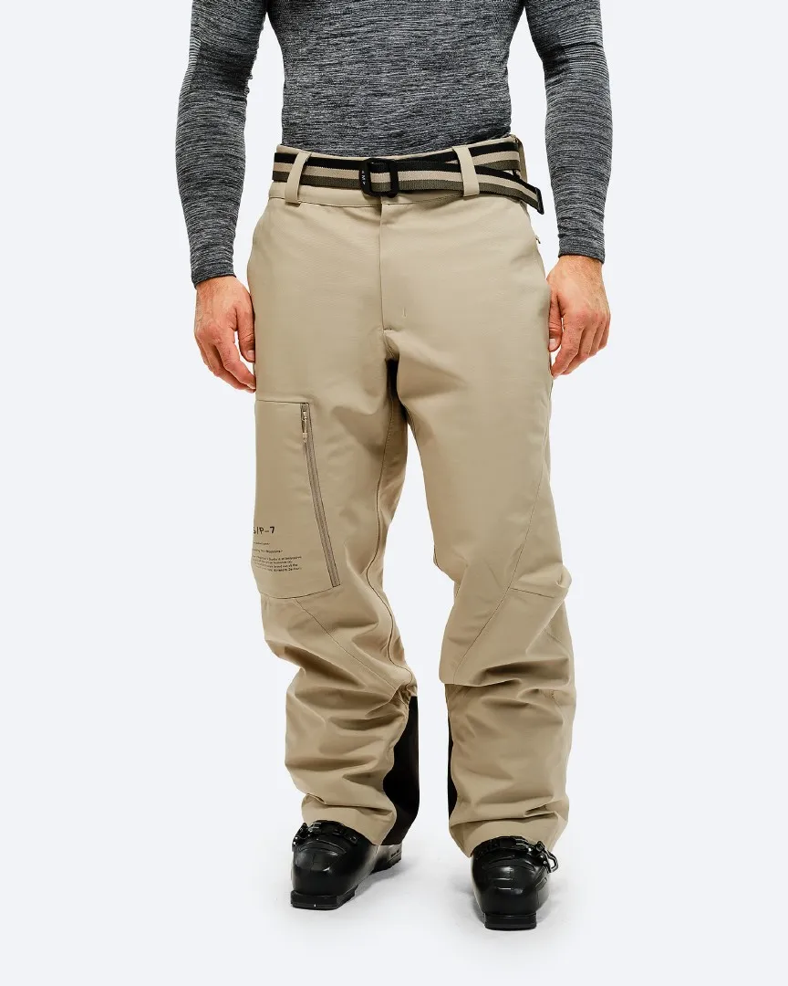 Person trägt eine P-7 Ride Insulated Pant in Seneca Rock, mit Skischuhen vor einem weißen Hintergrund.