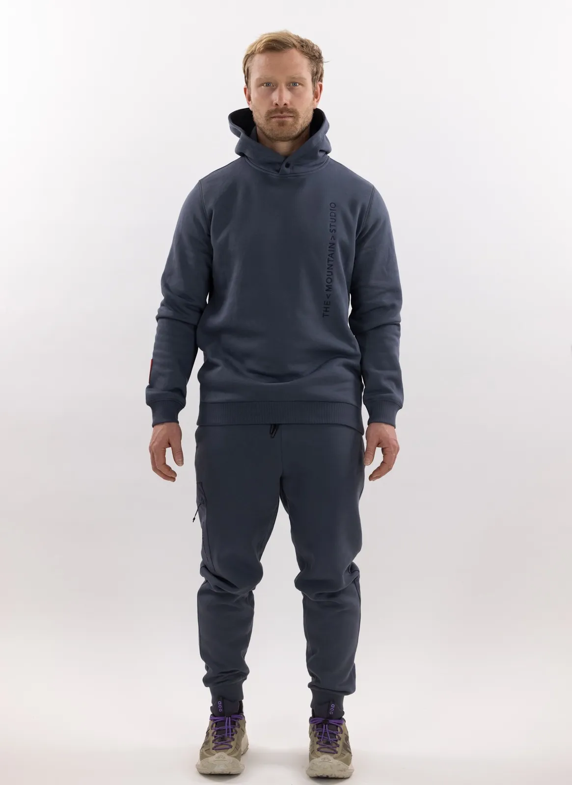 Mann in grauer Z-5 3L Hybrid Shell Jacket und passender Hose von The Mountain Studio vor weißem Hintergrund.