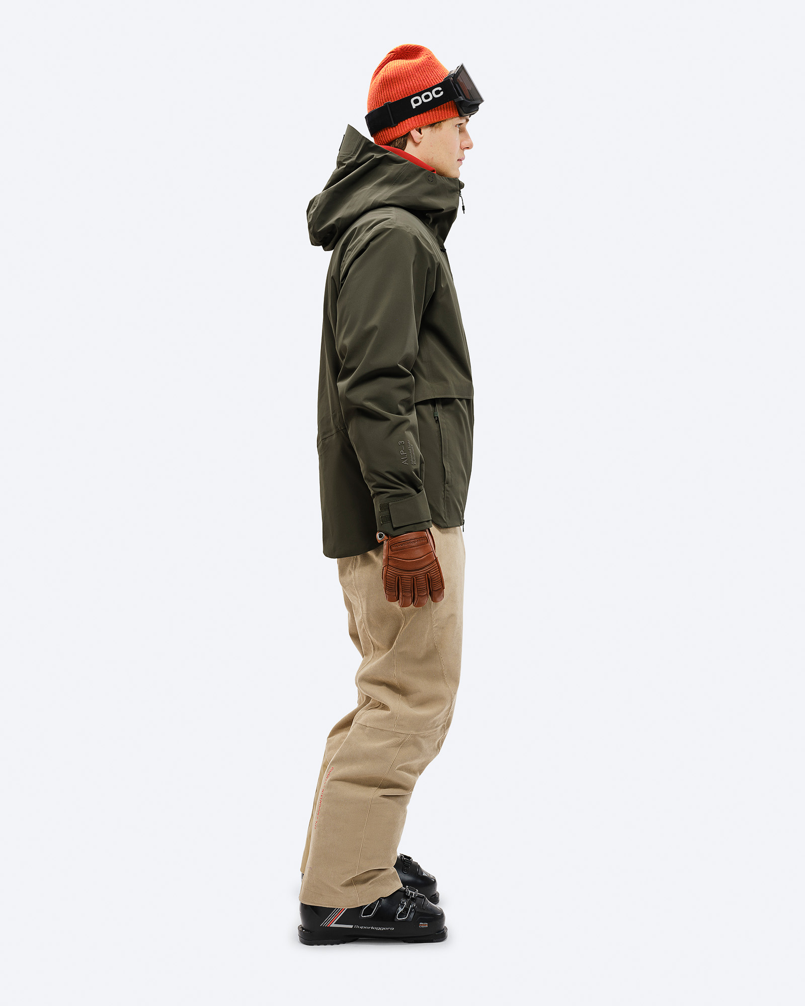 Ein Mann in seitlicher Ansicht, trägt eine grüne S-3 Carv Insulated Stretch Jacket, Skihose, Mütze und Skibrille.