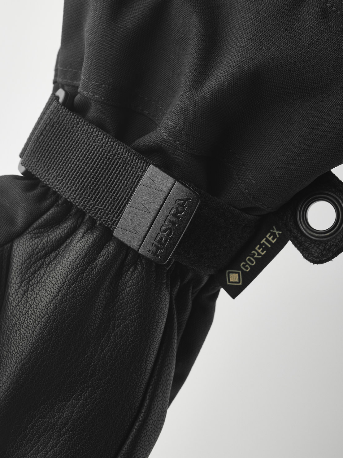 Nahaufnahme eines schwarzen Hestra-Handschuhs mit Gore-Tex-Etikett und verstellbarem Riemen. Das Material ist Leder und Textil.
