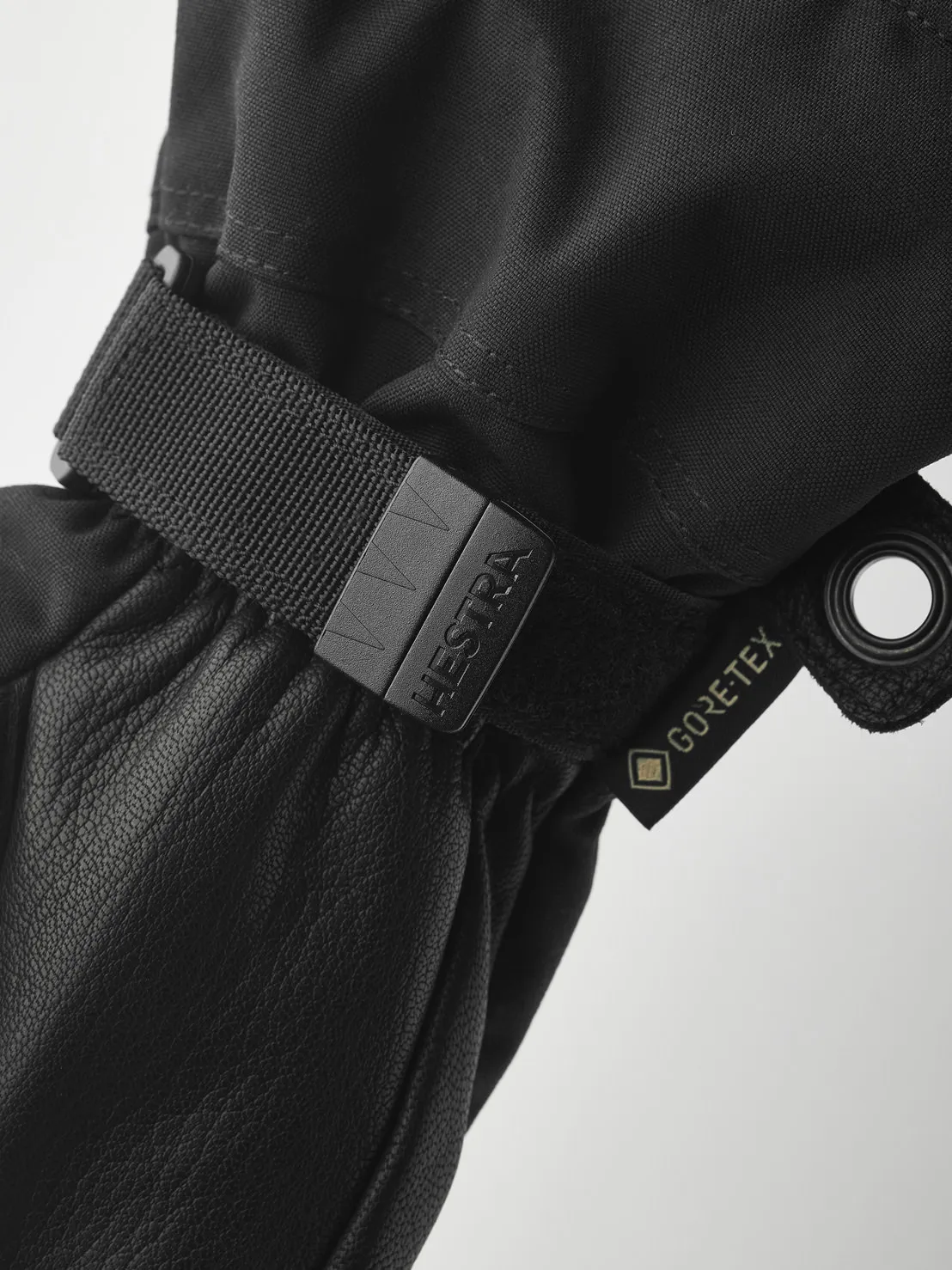 Nahaufnahme eines schwarzen Hestra-Handschuhs mit Gore-Tex-Etikett und verstellbarem Riemen. Das Material ist Leder und Textil.
