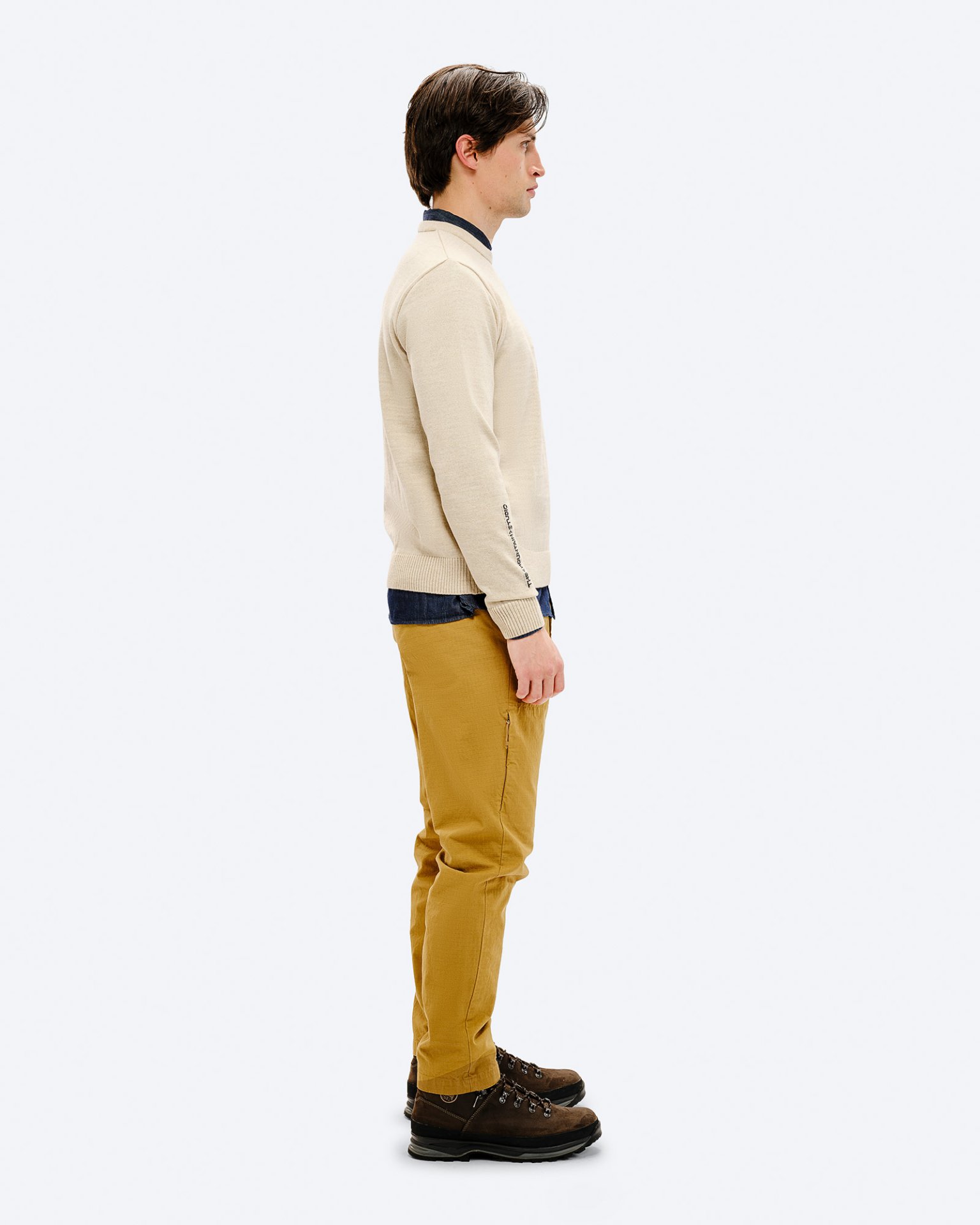 Ein Mann, von der Seite, trägt den K-3 ST Ski Sweater in Beige, kombiniert mit braunen Wanderschuhen und gelben Hosen.
