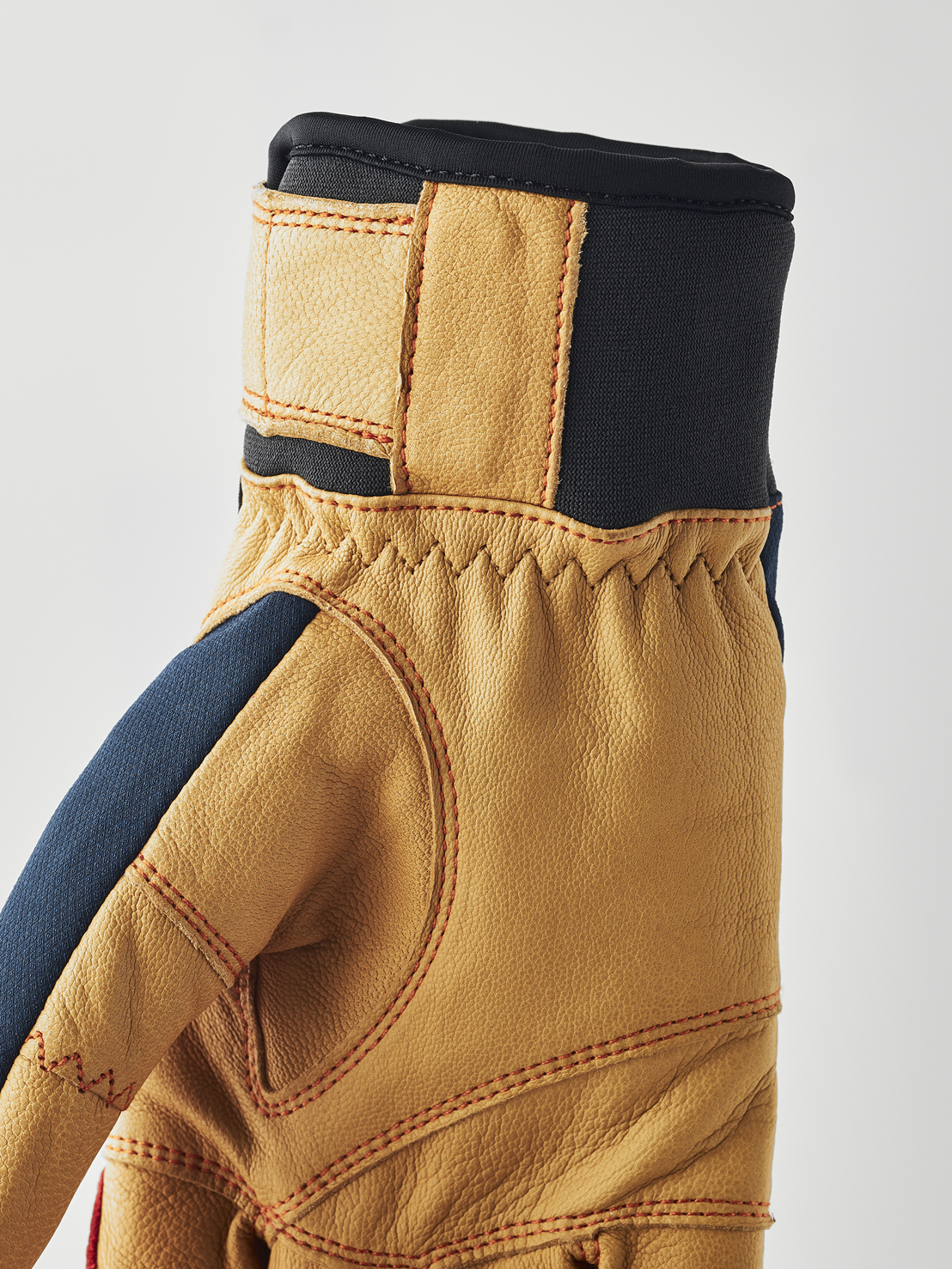 Lederhandschuh mit Akzenten Nahaufnahme eines hellbraunen Lederhandschuhs mit blauen Akzenten und roten Ziernähten, sowie einem schwarzen Bund.