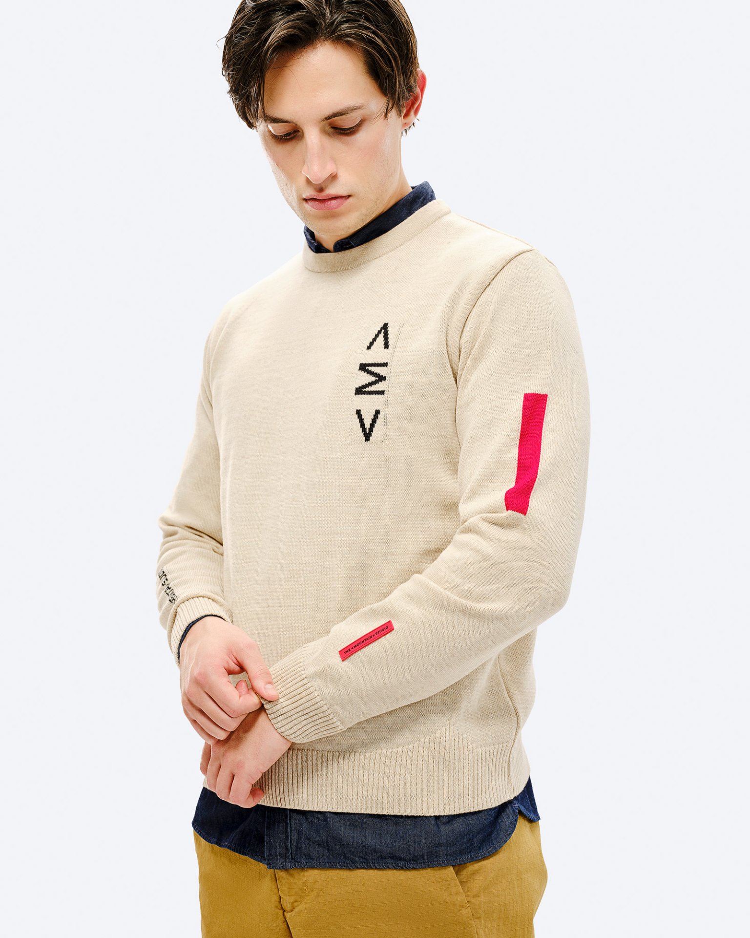Mann im Ski Sweater St. Moritz. Beiger Pullover mit rotem Detail am Ärmel und schwarzem Muster auf der Brust.