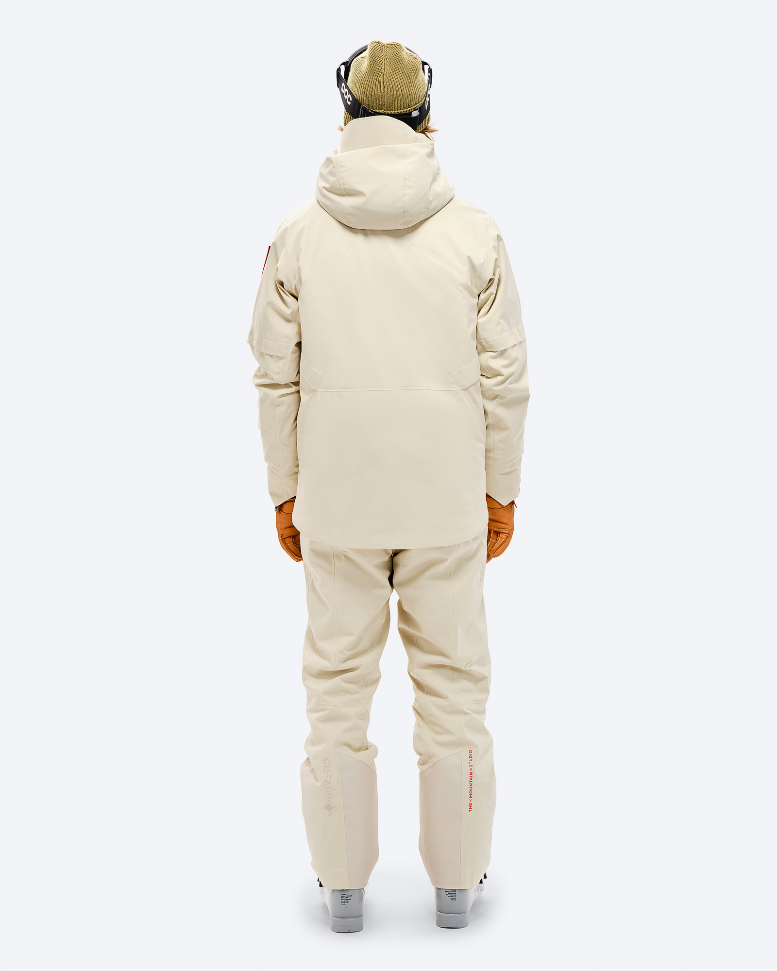 Person von hinten in beiger S-1 GORE-TEX 2L Stretch Insulated Jacke und passender Hose, braune Handschuhe, Skibrille und Mütze.