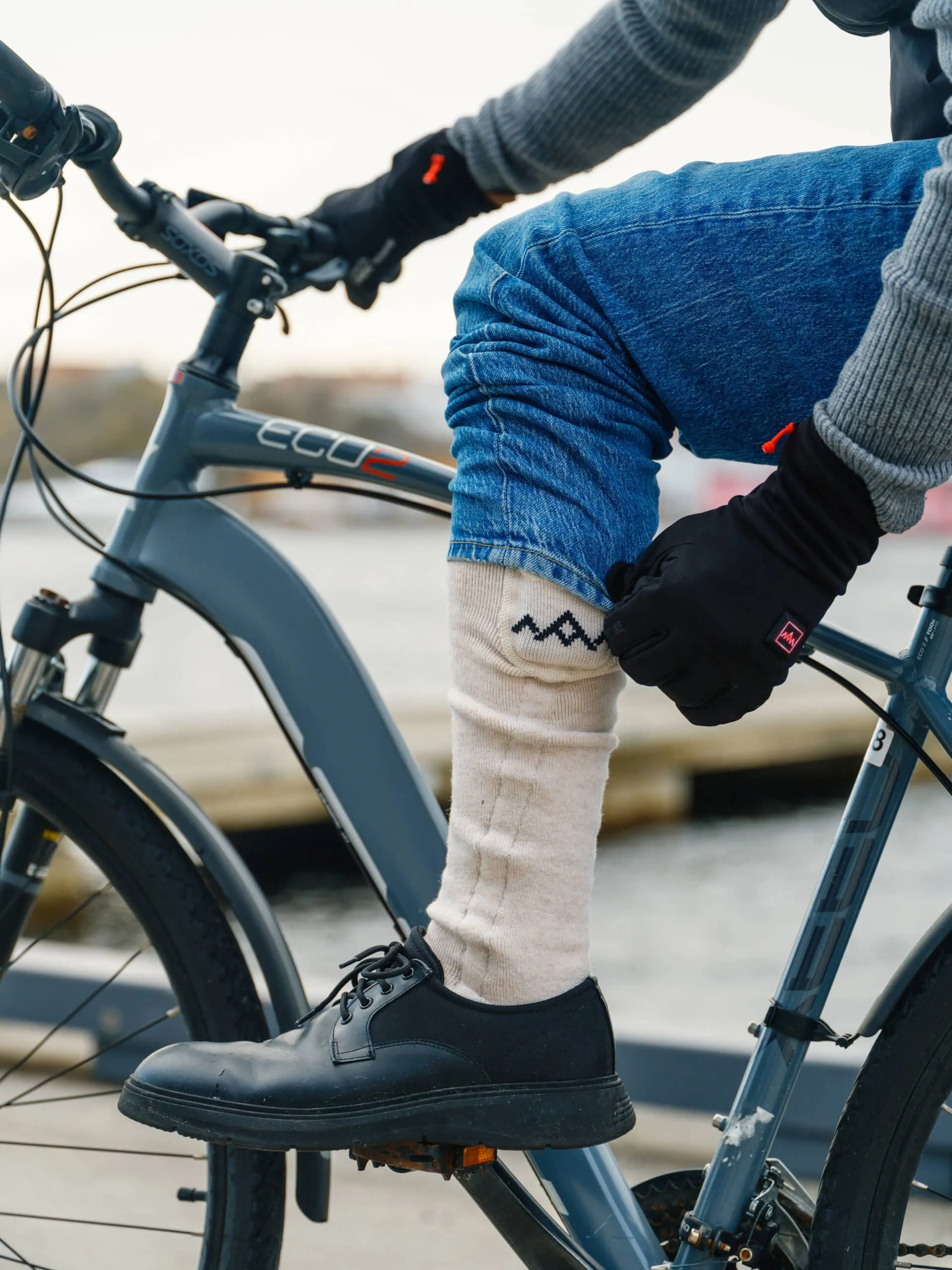 Person mit beheizten Socken und Handschuhen auf einem Fahrrad. Die Socke ist beige mit einem dunklen Zickzackmuster.