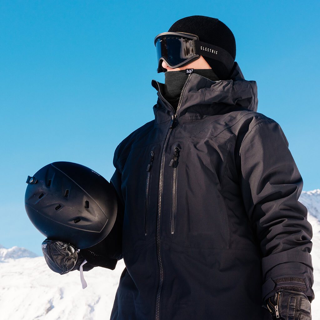 Mann in Winterlandschaft Ein Mann mit schwarzer Jacke, Beanie, Brille und Neckwarmer hält einen Helm in einer Winterlandschaft.