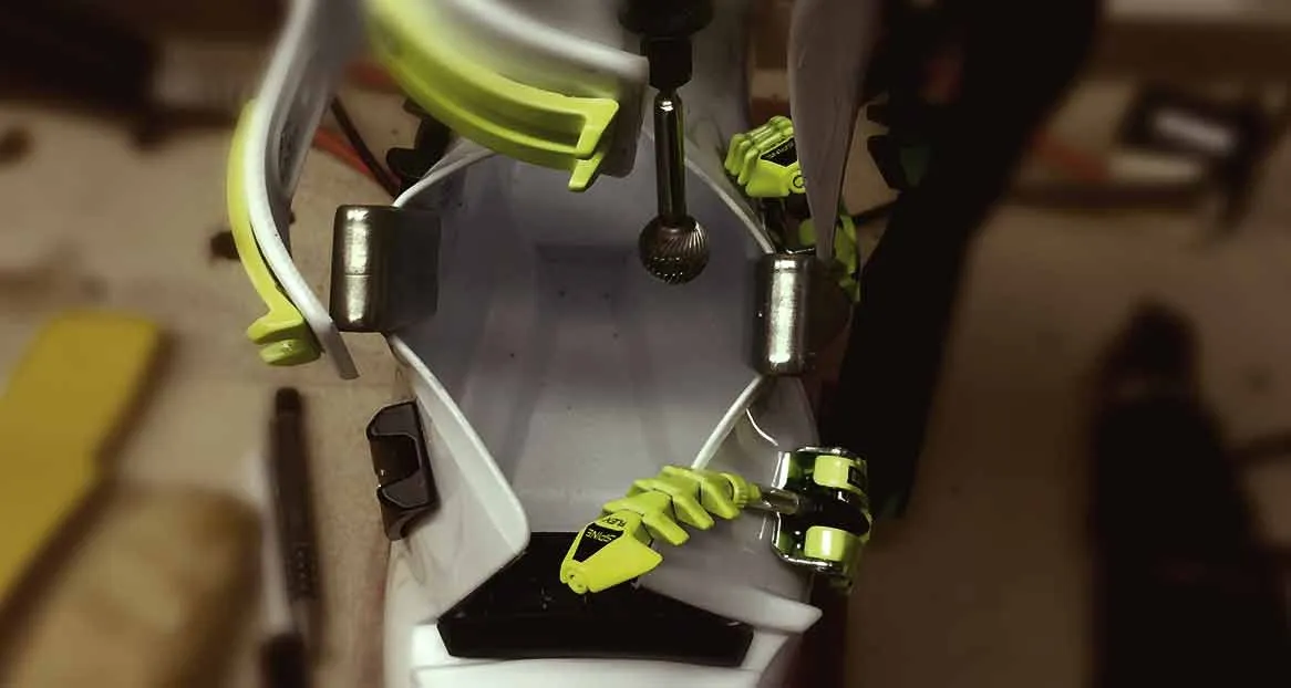 Ein Skischuh wird mit einem Fräser bearbeitet, um ihn an den Fuß anzupassen. Metallteile und gelbe Details sind sichtbar.