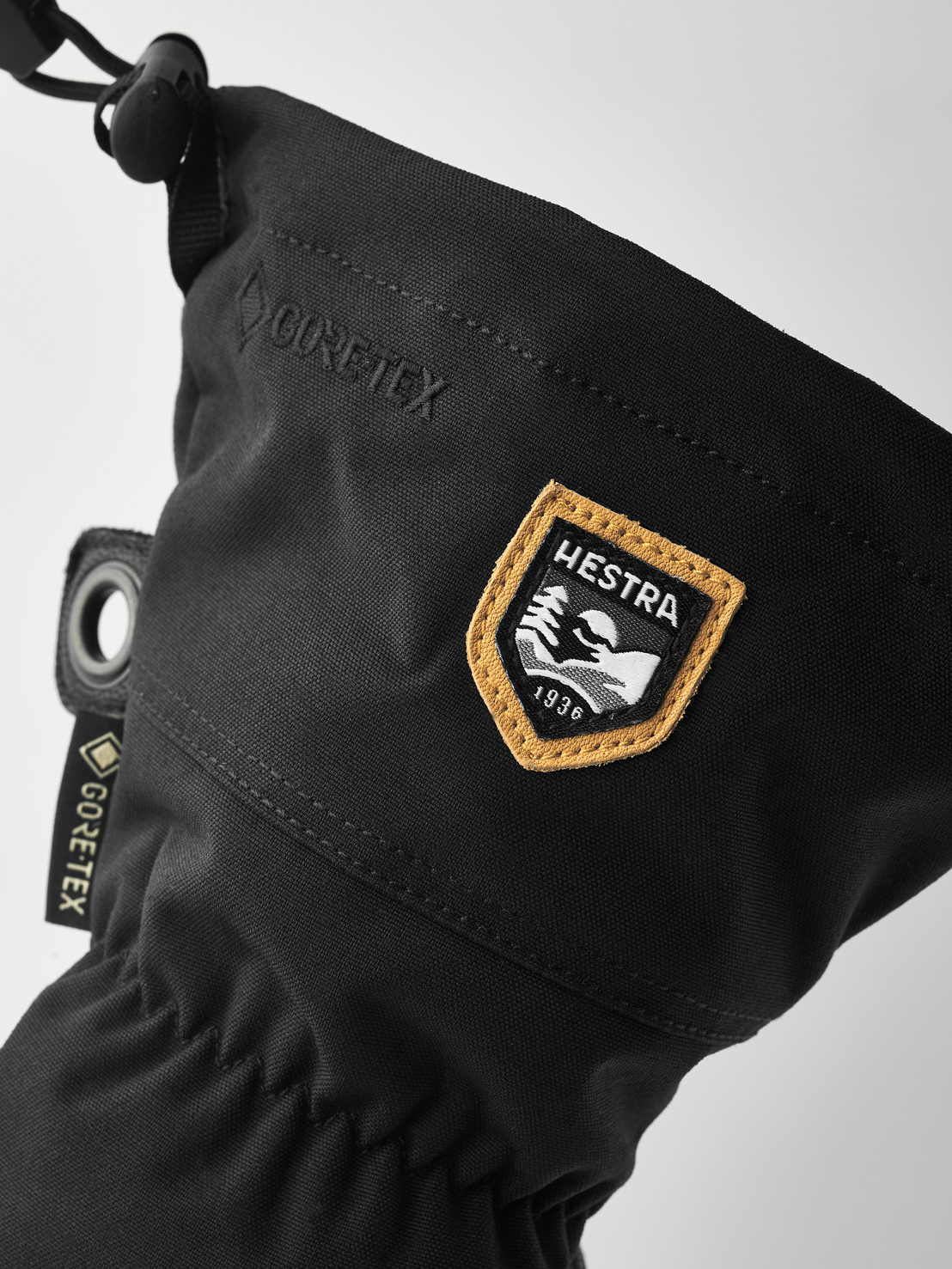 Hestra Army Leder Fäustlinge Detailaufnahme eines schwarzen Hestra Army Leather Gore-Tex Fäustlings mit Logos und Zugschnur.