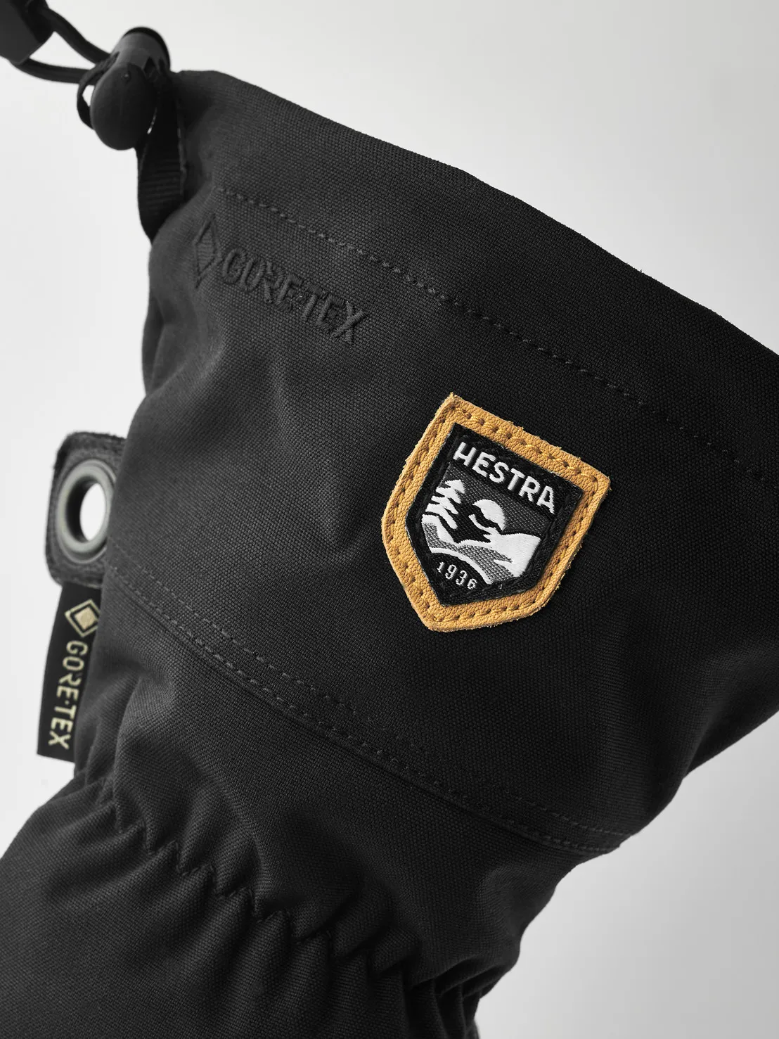 Detailaufnahme eines schwarzen Hestra Army Leather Gore-Tex Fäustlings mit Logos und Zugschnur.