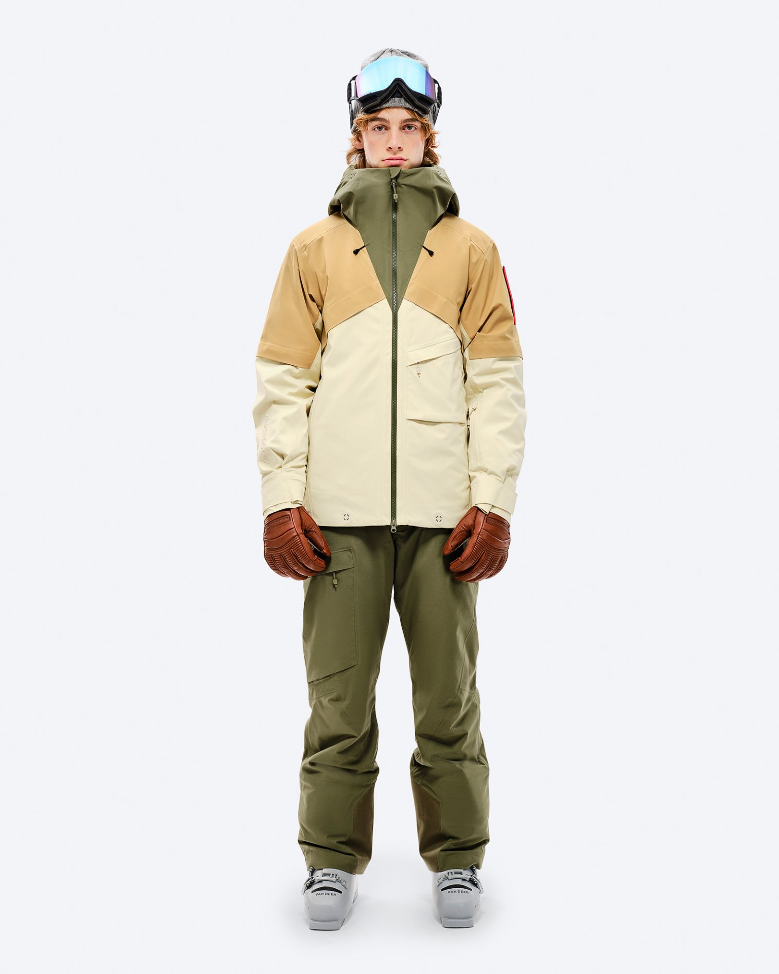 Person in Winterausrüstung: GORE-TEX Jacke in Beige/Braun, Winter Moss Hose, Handschuhe und Skibrille.