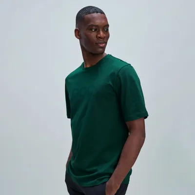 Ein junger Mann mit dunkler Hautfarbe trägt ein grünes T-Shirt mit kurzen Ärmeln und blickt über seine Schulter.