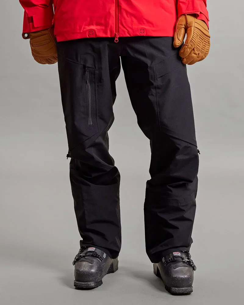 Vorderansicht einer schwarzen Y-1 HD GORE-TEX Pro 3L Shell Pant mit Skischuhen und Skihandschuhen auf grauem Hintergrund.