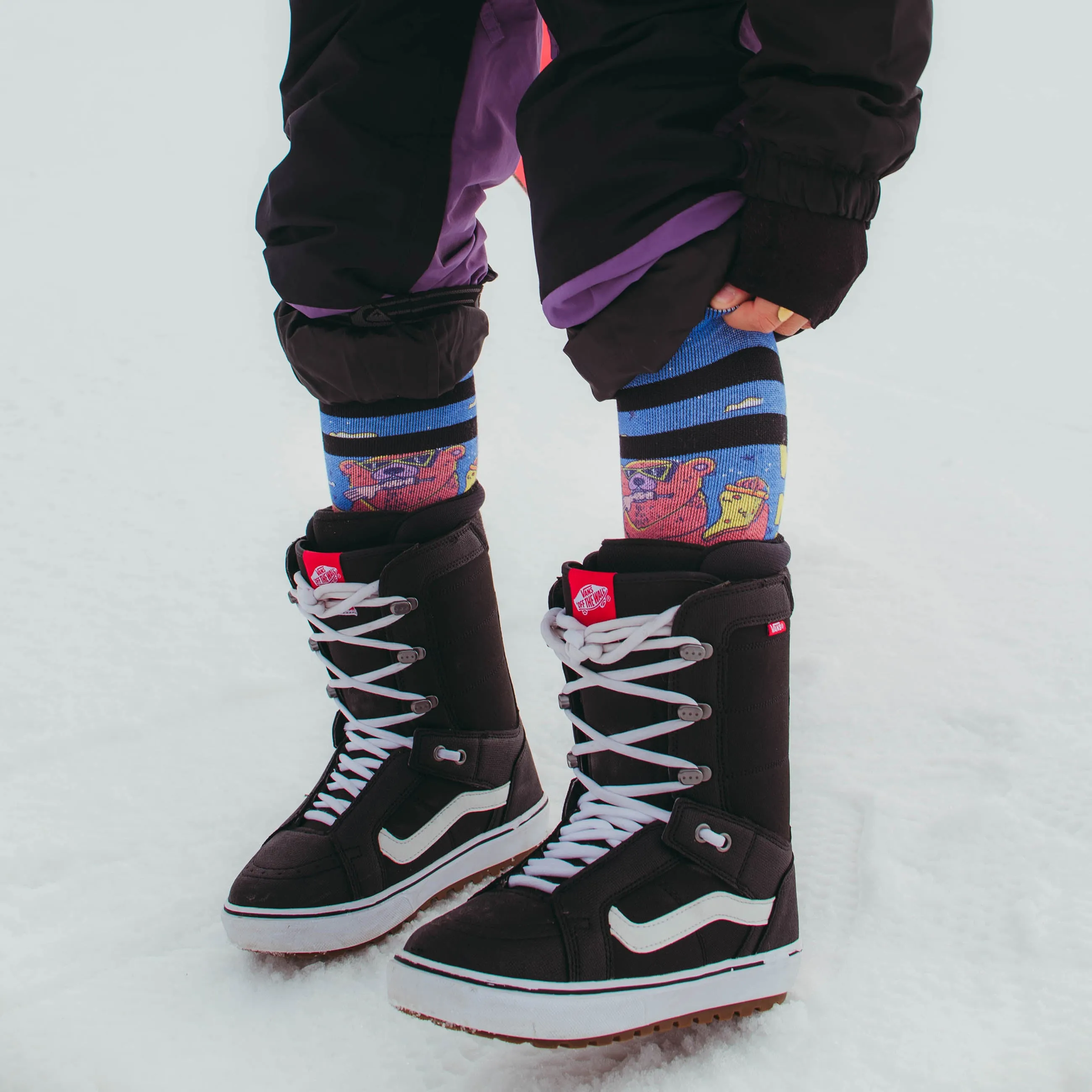 Person mit Snowboardstiefeln und Wild Nature Socken im Schnee. Socken mit Bärenmuster.