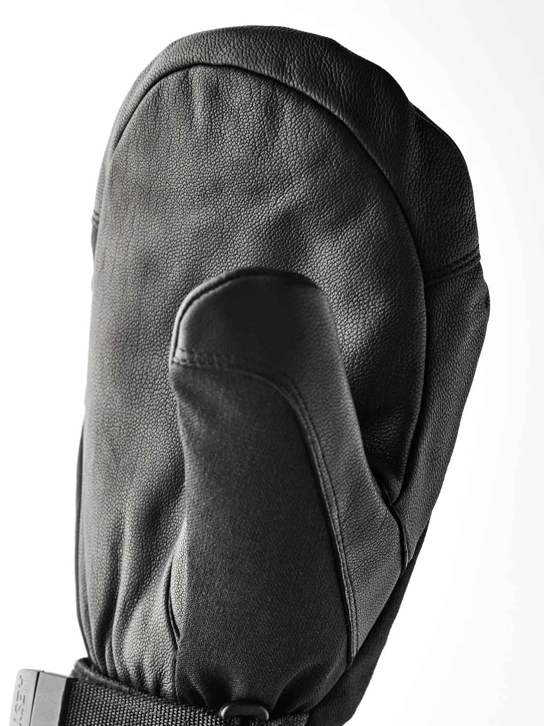 Eine schwarze, lederne Fäustlingshandschuh liegt auf einer weißen Fläche. Der Daumen ist nach vorne gerichtet und der Handrücken ist gewölbt.