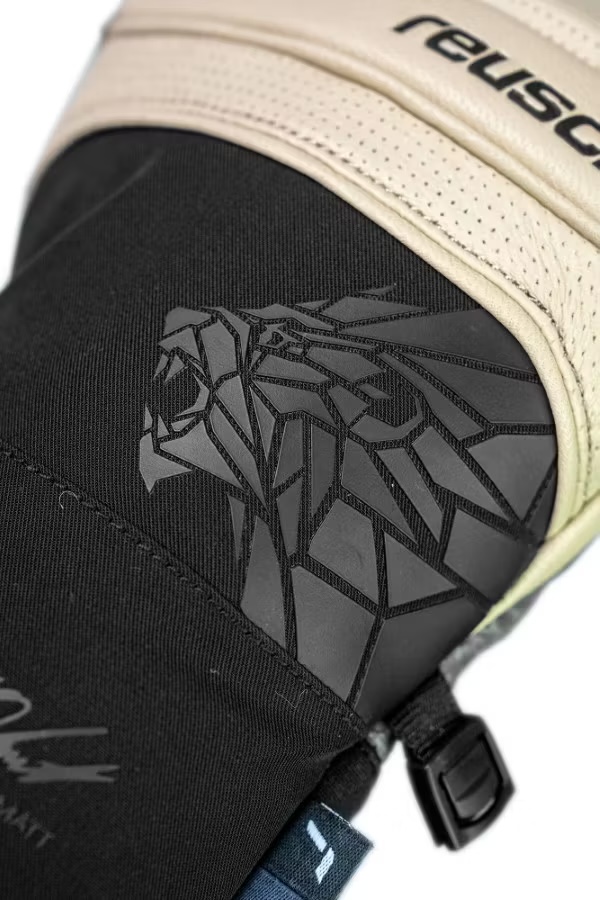 Geometrischer Löwenkopf-Handschuh Nahaufnahme eines Handschuhs mit geometrischem Löwenkopf-Design in Schwarz auf dunklem Stoff. Oben helles Leder mit Reusch-Schriftzug.