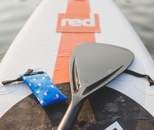 Blauer Flamingo Surfer Blauer Flamingo Sunnysoc auf Surfbrett mit Paddel. Sonnenbrillen Schutz.