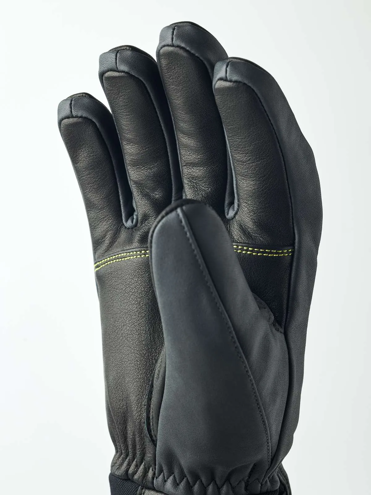 Schwarzer Hestra Omni Trigger Handschuh von Nahem, die Hand ist leicht geöffnet und zeigt die Finger. Gelbe Nähte sind sichtbar.