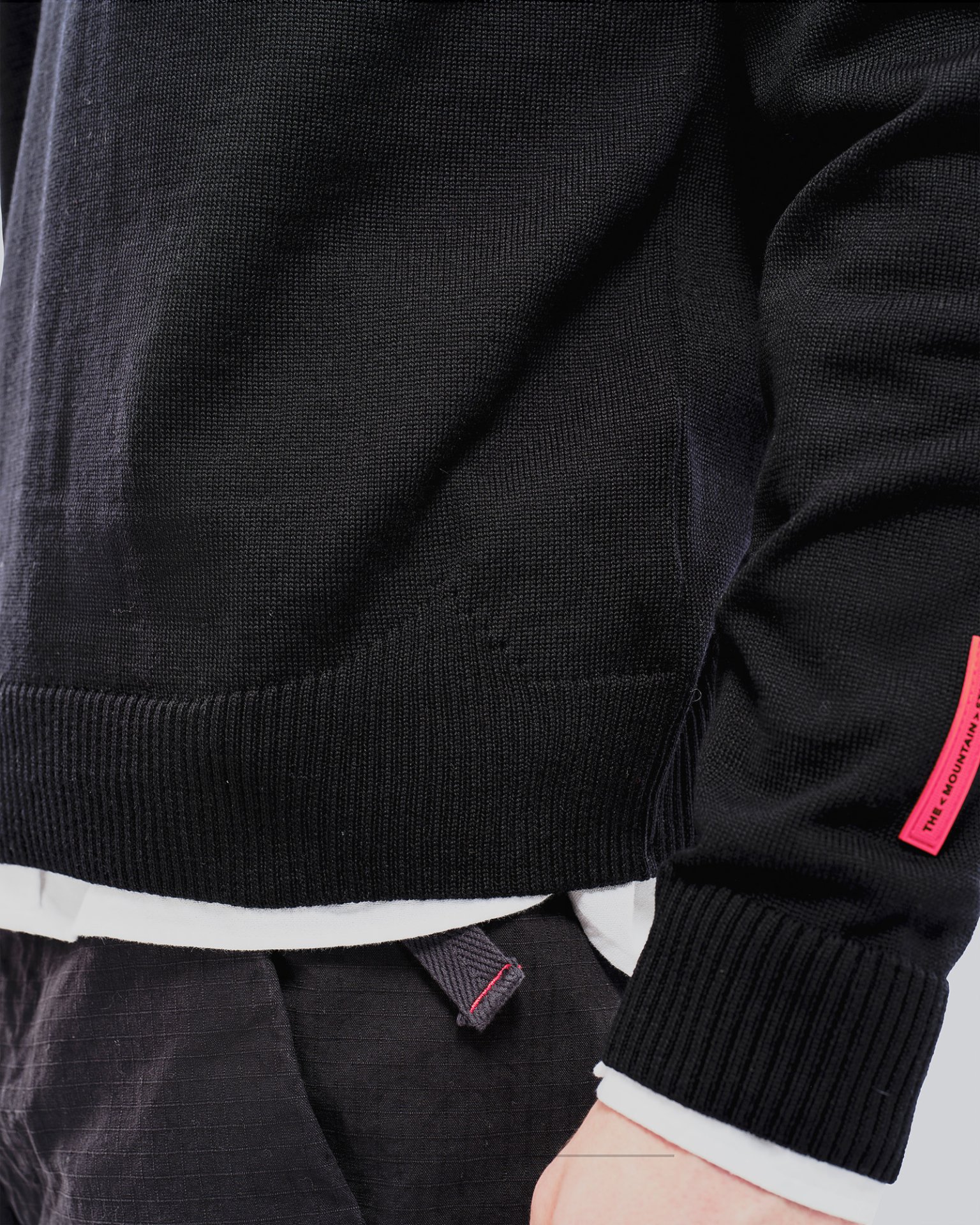 Nahaufnahme eines schwarzen K-3 Ski Pullovers aus Merinowolle mit Rundhalsausschnitt und rotem Etikett.