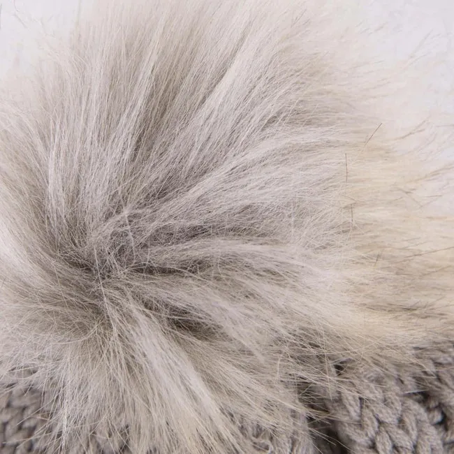 Detailaufnahme einer grauen Strickmütze mit großem, buschigem Bommel in Grau- und Weißtönen.
