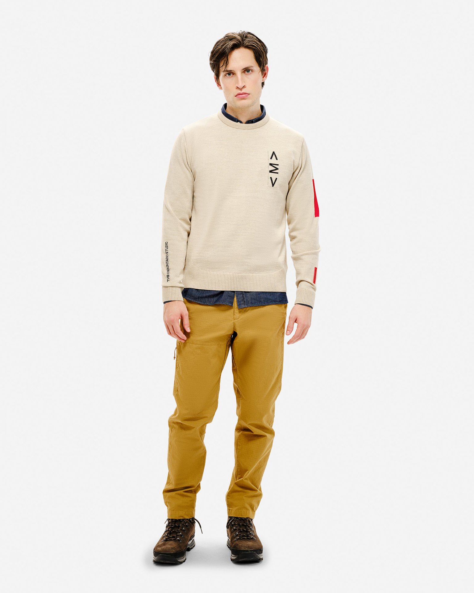 Mann trägt beigen Ski Sweater mit Muster, braune Hose und Schuhe vor einem weißen Hintergrund.