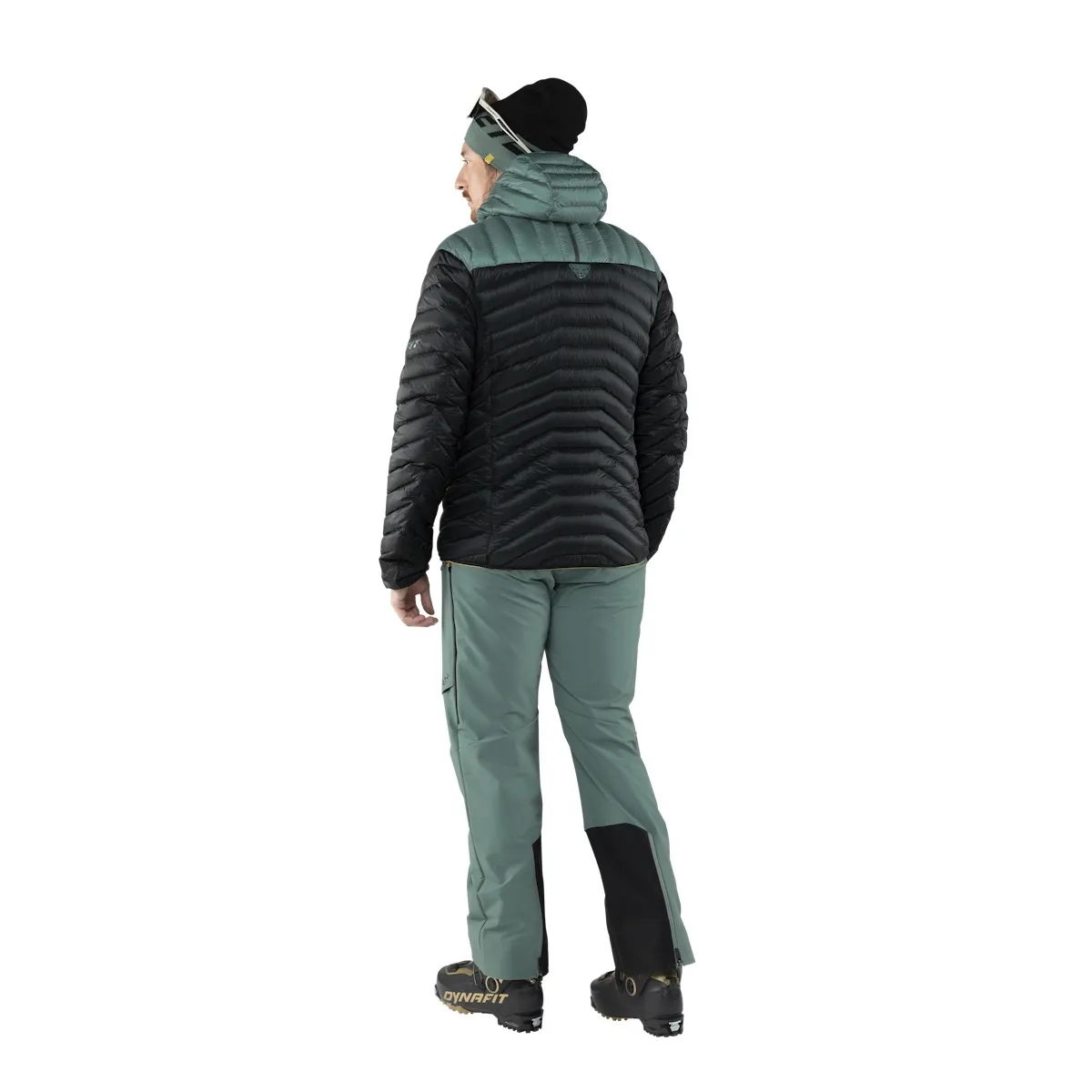 Rückansicht: Person mit Dynafit Ridge Ultralight Daunenjacke in Schwarz und Grün. Ski-Hose, Mütze und Skischuhe.