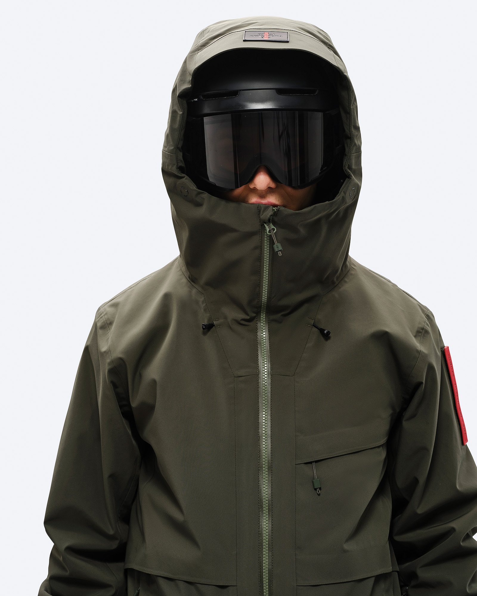 Person in Ski-Jacke "Forest Green" mit Kapuze und Skibrille. Frontalansicht bis zur Hüfte.