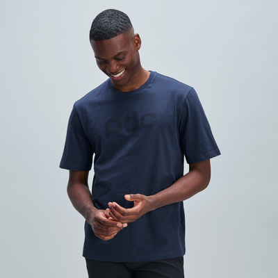 Lächelnder Mann im T-Shirt Ein lächelnder, dunkelhäutiger Mann trägt ein dunkelblaues T-Shirt mit dem Schriftzug "poc" und berührt seine Hände.