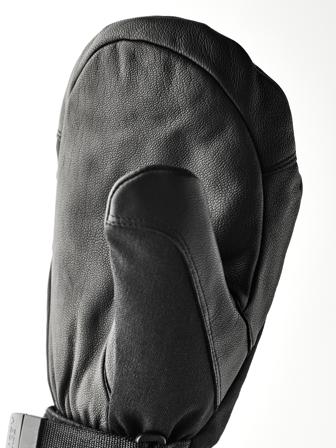 Eine schwarze, lederne Fäustlingshandschuh liegt auf einer weißen Fläche. Der Daumen ist nach vorne gerichtet und der Handrücken ist gewölbt.