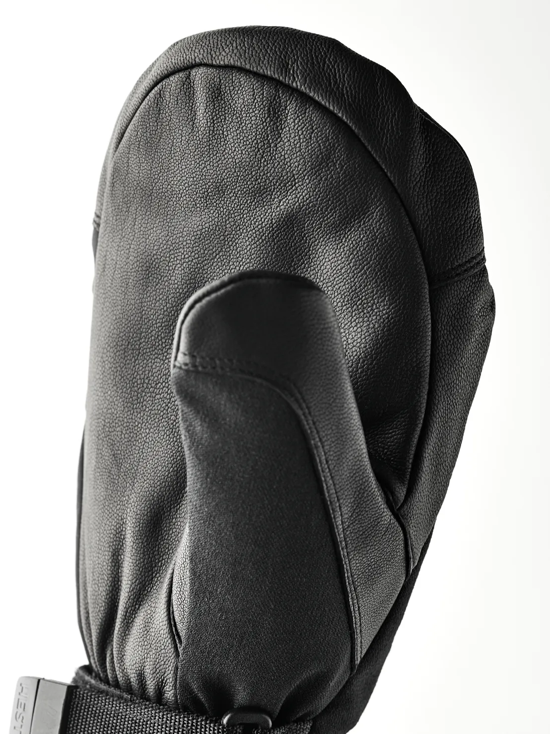 Eine schwarze, lederne Fäustlingshandschuh liegt auf einer weißen Fläche. Der Daumen ist nach vorne gerichtet und der Handrücken ist gewölbt.